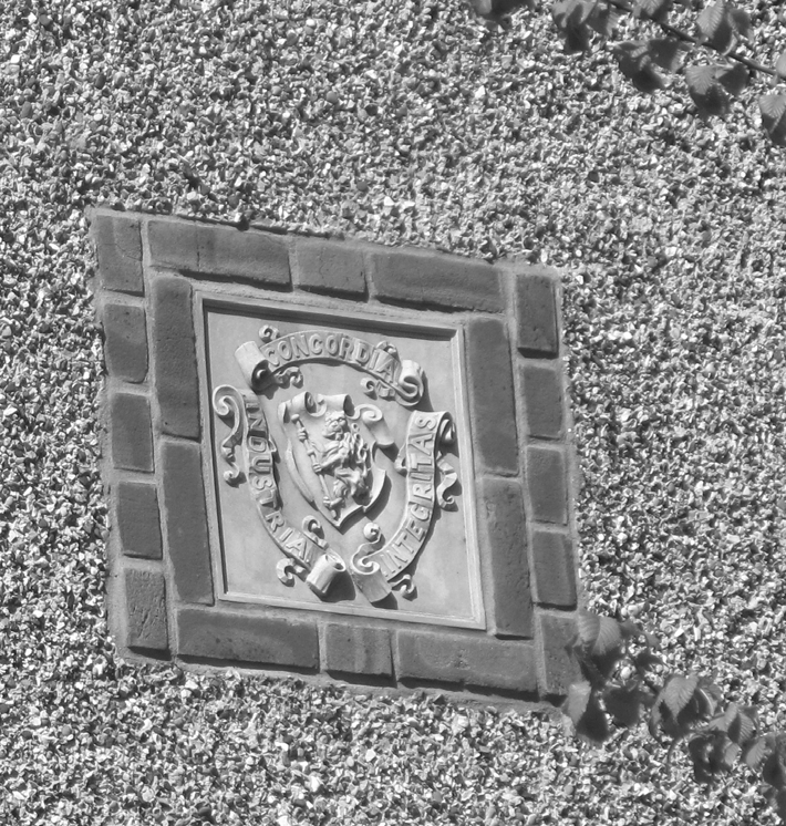 A stone-carved coat of arms reading Concordia, Industria, Integritas, set into a pebble-dashed wall